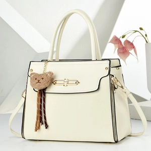 Detailed macro view of cream leather handbag featuring gold clasp and brown bear charm