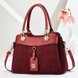Elegant burgundy patchwork corduroy handbag with gold clover charm on a white pedestal