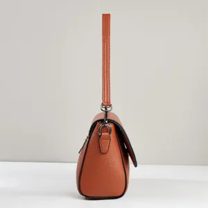 Side view of orange-brown litchi texture flap bag showing metal buckle and leather strap