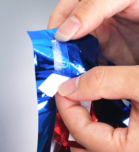 Detail der selbstklebenden Rückseite, die vom rot-blauen Metallic-Folienvorhang abzieht