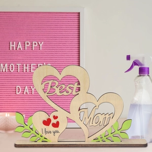 Detail of wooden Best Mom ornament with cutout letters and red heart on light surface