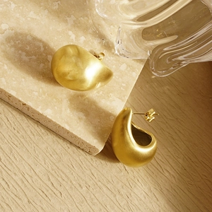 Close-up of golden teardrop earrings with a matte frosted texture on a stone background