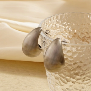 Close-up of matte silver water drop earrings on a textured glass rim with silk background