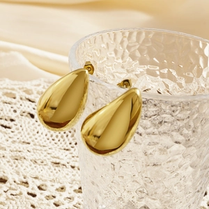 Close-up of golden teardrop earrings hanging on a glass rim with silk background