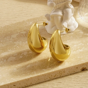 Elegant gold teardrop earrings in polished stainless steel on a marble stone background