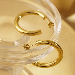 Close-up of high-polished gold C-shaped hoop earrings on a ribbed glass tray