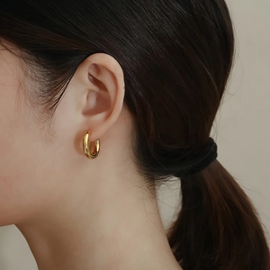 Close-up of a polished golden C-shaped hoop earring worn on a model's ear