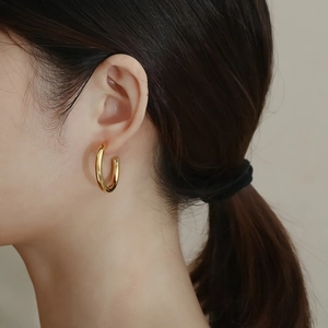Detailed view of model wearing gold C-shaped titanium steel earrings with a polished finish