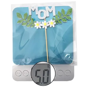 Detail of glitter MOM cake topper with silver letters, green leaves and white daisies