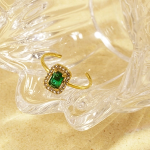 Detail of adjustable gold ring with emerald-cut green stone and pavé zircon border