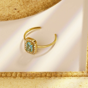 Macro detail of adjustable gold ring with emerald cut blue stone and pavé halo
