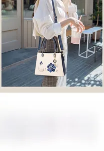 Detail showing blue floral butterfly embroidery on a cream leather tote with heart charm