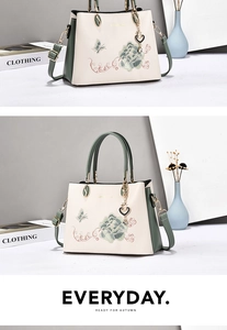 Detail of peony embroidery and heart pendant on a two-tone top-handle crossbody bag