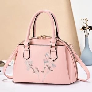 Close-up of elegant floral embroidery and golden dual zippers on a light pink shell bag