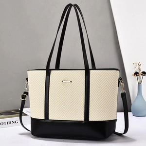 Detail of herringbone weave tote bag with black leather handles and gold metal hardware
