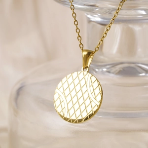 Minimalist gold stainless steel tennis pendant necklace hanging on glass with natural lighting