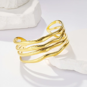 Dettaglio del bracciale rigido dorato a fascia larga con linee metalliche ondulate