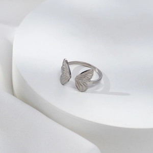 Minimalist stainless steel open butterfly wing ring on a white geometric stand