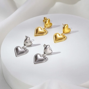 Zweischichtige Herz-Ohrhänger in Gold und Silber auf einem weißen Steinsockel aus Edelstahl