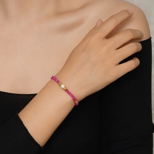 Détail du bracelet en perles facettées magenta avec perle centrale porté au poignet