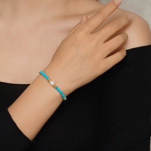 Détail du bracelet en perles de turquoise avec perle blanche et accents dorés au poignet