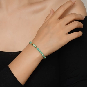 Gros plan d'un bracelet en perles de turquoise avec perles dorées porté au poignet