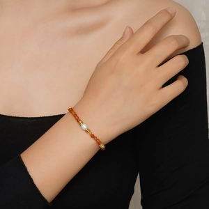 Détail d'un bracelet en perles avec des pierres orange et une perle baroque blanche au poignet