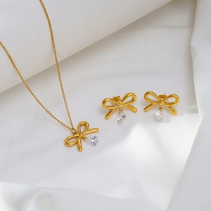 Golden bow necklace and earrings set with white drop zircon on white silk fabric