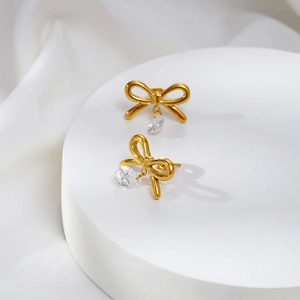 Elegant gold bow earrings featuring teardrop zircon crystals on a white display stand