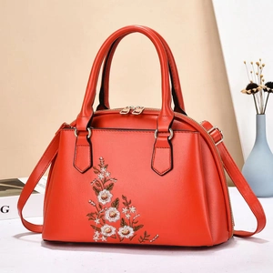Close-up of floral embroidery on a trapezoid red PU handbag with gold hardware