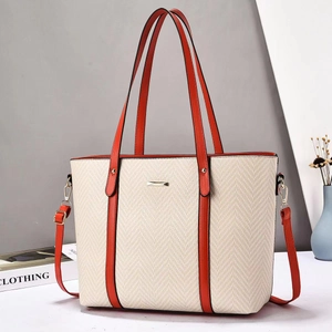 Close-up of beige herringbone tote bag with orange leather handles and gold hardware logo