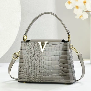 Detail of grey crocodile pattern handbag with gold V-shaped logo and metallic hardware