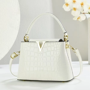 Detail of white crocodile texture handbag featuring a prominent gold V-shaped metal logo