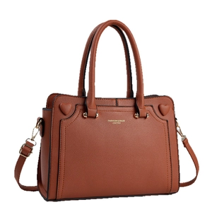 Brown leather tote bag with heart decor and adjustable strap on white background