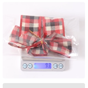 Detailed view of red and black plaid Christmas bow being weighed on a digital scale