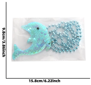Detail eines Delfin-Anhängers mit Pailletten und Maßangaben in cm und Zoll