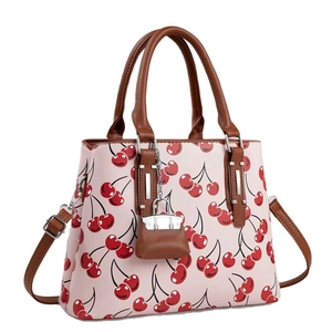 Pink tote bag with red cherry print featuring brown handles and a mini bag charm