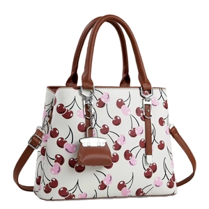 White crossbody bag with cherry prints, brown leather straps and a mini bag charm