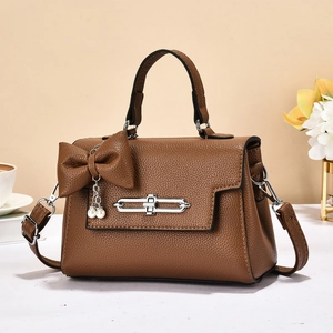 Classic brown pebble leather handbag with bow and pearl detail on a desk