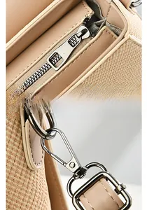 Detail of light gold metal zipper and swivel hook on beige woven leather handbag