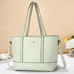Detail of mint green tote bag featuring golden logo plate and adjustable shoulder straps