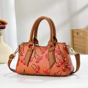 Detail of cherry print tote bag featuring brown handles and golden metal hardware