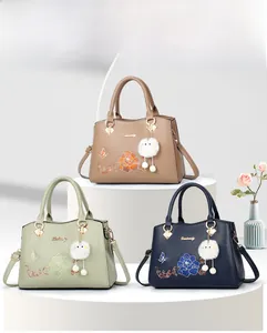 Detailed view of floral embroidery and pompom charm on middle-aged women's PU handbags