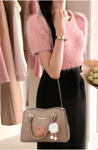 Detail of floral embroidery and white plush pendant on brown crossbody bag for elderly women