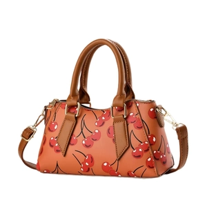 Orange-brown leather handbag with vibrant red cherry patterns and gold hardware