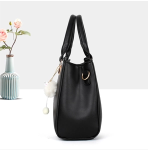 Detailed side view of a black PU leather handbag for elderly women with white pompom charm