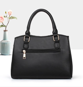Detail of black faux leather handbag with golden metal hardware and front zip pocket