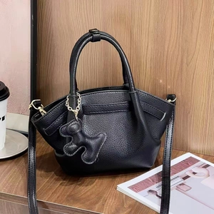 Close-up of black lychee grain leather handbag with golden hardware and dog-shaped charm