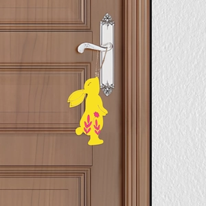 Detail of yellow rabbit wooden pendant with pink floral patterns hanging on a door handle