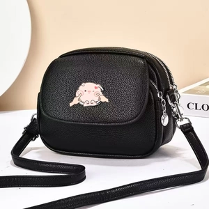 Détail du sac à bandoulière noir en cuir grainé avec petit cochon rose et zips argentés